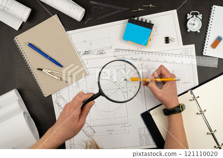 Look through a magnifying glass. Mechanical drawing on sheets of paper. Hands on the table top view. Workflow of an architect, engineer. Write and draw. Ruler, pencil, notebook 121110020