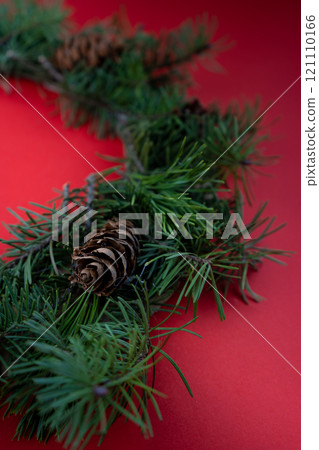 Christmas wreath from coniferous fir branches. New Year's decor. A wreath of green branches and cones on a red background. Copy space. 121110166