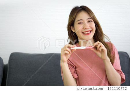 Happy pregnant young asian woman expectant mother holding pregnancy test stick checking positive result expecting baby after ivf fertility infertility treatment in vitro fertilization concept 121110752