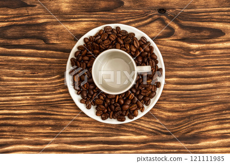 On the saucer is a cup of an empty cup for coffee and lie coffee beans 121111985
