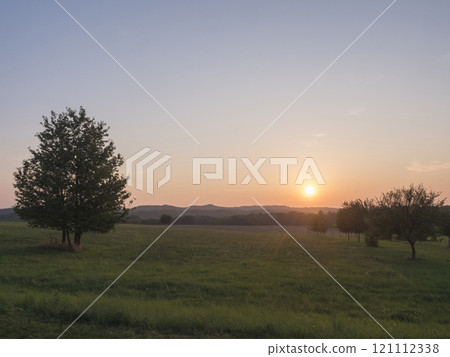 Orange sunset over green summer meadow and forest with alone cherry tree and deciduous tree alley, clear sky background, Countryside landscape, copy space, Kokorin region, central Bohemia Orange sunset over green summer meadow and forest with alone cherry tree and deciduous tree alley, clear sky background, Countryside landscape, copy space, Kokorin region, central Bohemia 121112338