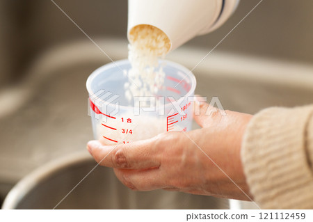 A woman measuring the amount of rice with a measuring cup A woman measuring the amount of rice with a measuring cup 121112459