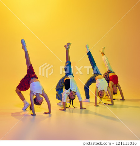 Four flexible and talented girls, teenagers in casual cloches dancing, performing hip hop moves against yellow background in neon light 121113016