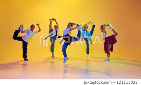 Youth culture. Group of teen girls, friends wearing casual clothes, dancing hip hop, learning new moves against yellow background in neon light Youth culture. Group of teen girls, friends wearing casual clothes, dancing hip hop, learning new moves against yellow background in neon light 121113022