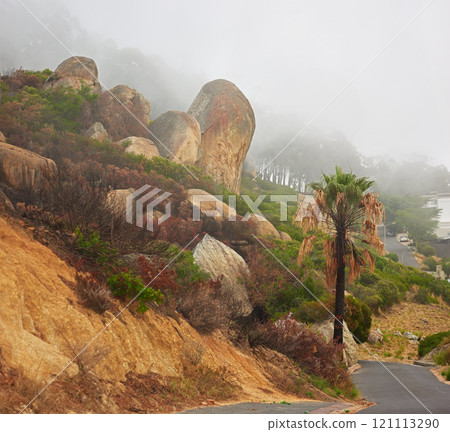 Rocky landscape along a road with thick smoggy air from a wildfire spreading and destroying trees and bushes, environmental damage. Big boulders on a scenic path in Cape town on a misty morning. 121113290