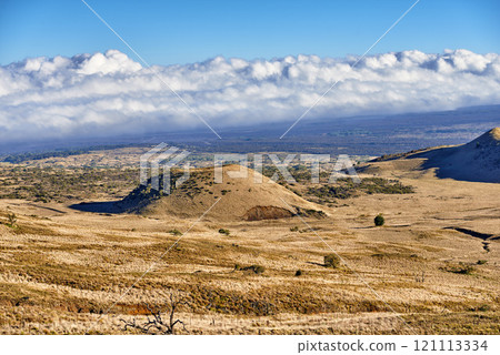 Volcano crater with copy space on a cloudy horizon. High angle view of an empty barren nature scene of desert grass fields over a mountain in Mauna Loa, Hawaii. Undisturbed hills for hiking adventure 121113334