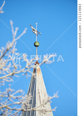 Spire of the church above the trees. Church spires against the cloudy sky in a blue sky. Close up of a spire in an autumn season with a clear sky in the background. A branch of a tree without leaves. Spire of the church above the trees. Church spires against the cloudy sky in a blue sky. Close up of a spire in an autumn season with a clear sky in the background. A branch of a tree without leaves. 121113663
