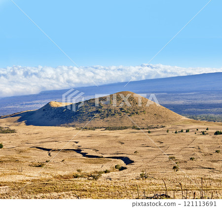 Copy space with a volcano crater on a cloudy blue horizon. Empty barren nature scene of dry grass fields over a mountain and a hiking trail. High angle background of Mauna Loa in Hawaii 121113691