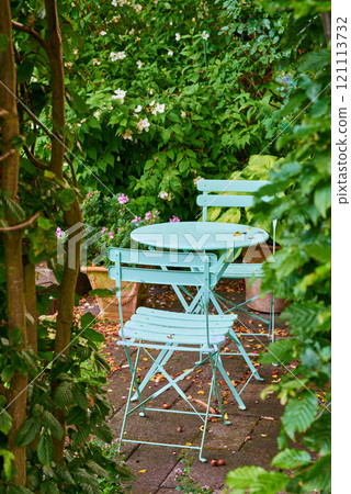 Two green metal chairs and table in a serene, peaceful private courtyard in a home backyard on a summer day. Small outdoor patio furniture set, seating in empty and tranquil garden with fresh plants Two green metal chairs and table in a serene, peaceful private courtyard in a home backyard on a summer day. Small outdoor patio furniture set, seating in empty and tranquil garden with fresh plants 121113732