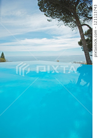 An outdoor infinity pool with copy space. Low angle of an empty swimming pool with clean, clear water surrounded by green trees and a blue sky. Luxury pool at a holiday resort or tourism guesthouse An outdoor infinity pool with copy space. Low angle of an empty swimming pool with clean, clear water surrounded by green trees and a blue sky. Luxury pool at a holiday resort or tourism guesthouse 121113743