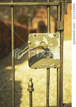 Old rural house wrought iron entrance gate with handcrafted grilles and an antique metal handle. Decorative antique door knob of the ancient craft hand-made iron door knob. Traditional entrance gate 121113849