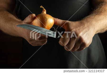 In a cozy kitchen, a person focuses on expertly slicing an onion. The soft glow from nearby lighting highlights their hands and the gleaming knife as they prepare for a delicious meal In a cozy kitchen, a person focuses on expertly slicing an onion. The soft glow from nearby lighting highlights their hands and the gleaming knife as they prepare for a delicious meal 121114317