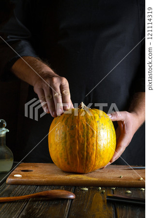 A skilled chef gently inspects a bright orange pumpkin resting on a wooden cutting board, surrounded by kitchen tools and an olive oil bottle, preparing for a seasonal recipe A skilled chef gently inspects a bright orange pumpkin resting on a wooden cutting board, surrounded by kitchen tools and an olive oil bottle, preparing for a seasonal recipe 121114319