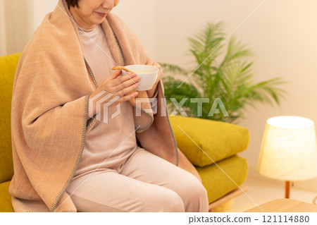 A middle-aged woman eating potage soup in the living room on a winter night 121114880