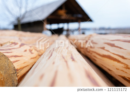 Close-up view of wooden logs with a workshop in the background, highlighting the textures and natural patterns of the wood 121115172