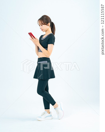 Full-body photo of a woman wearing sportswear and looking at her smartphone Full-body photo of a woman wearing sportswear and looking at her smartphone 121115587
