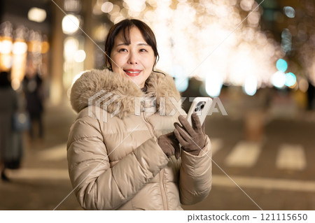 一位女士拿著智慧型手機，看著燈光 121115650