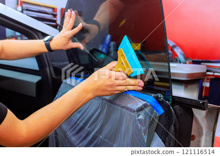 Technician applies window tint to car door while ensuring smooth finish in vibrant auto repair environment. Technician applies window tint to car door while ensuring smooth finish in vibrant auto repair environment. 121116514