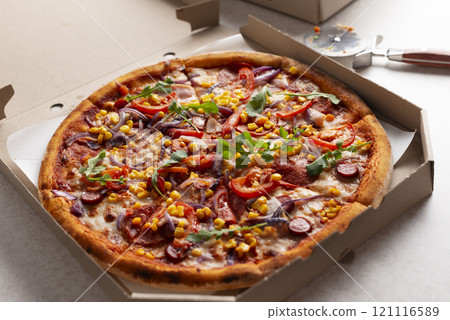 Large Pizza in open carton box and cutter on kitchen table closeup view 121116589