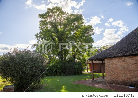 Charming heritage building surrounded by lush trees and greenery under a sunny sky Charming heritage building surrounded by lush trees and greenery under a sunny sky 121116712