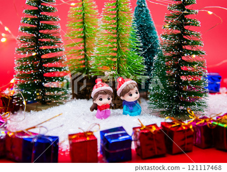 Dolls sit in the snow among Christmas trees and presents 121117468