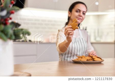Beautiful woman holding plate of delicious gingerbread cookies in the kitchen, focus on cookies. Christmas time 121117830