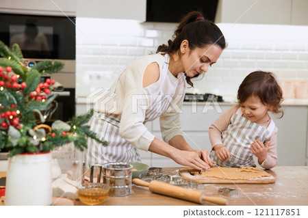 Happy mother and little child daughter cutting cookies of raw gingerbread dough in kitchen. Christmas time 121117851