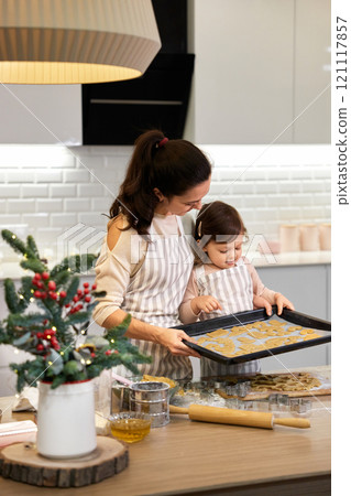 happy mother and little child daughter holding tray with gingerbread cookies in kitchen. Christmas time 121117857