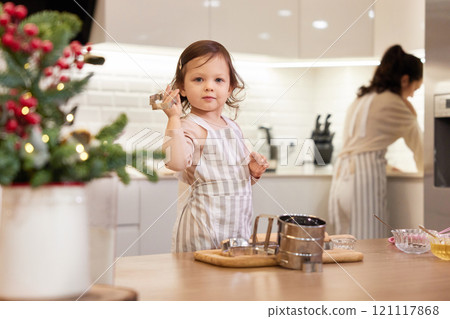 smiling little child girl in apron baking cookies in the kitchen 121117868