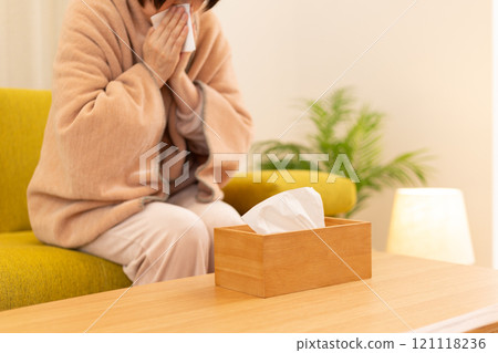 A middle-aged woman blowing her nose in the living room on a winter night A middle-aged woman blowing her nose in the living room on a winter night 121118236