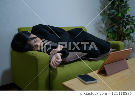 A woman living alone falls asleep on the sofa while looking at a tablet, businesswoman, overtime, long working hours 121118585