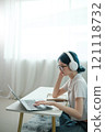 A woman wearing headphones and glasses is typing on a laptop 121118732