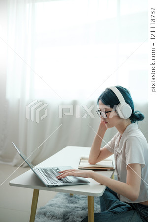A woman wearing headphones and glasses is typing on a laptop A woman wearing headphones and glasses is typing on a laptop 121118732