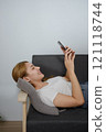 A woman is laying on a couch and looking at her phone 121118744