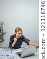 A woman is sitting at a desk with a laptop open 121118746