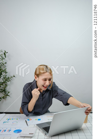 A woman is sitting at a desk with a laptop open A woman is sitting at a desk with a laptop open 121118746