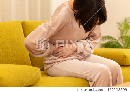A middle-aged to senior woman suffering from stomach pain in the living room on a winter night A middle-aged to senior woman suffering from stomach pain in the living room on a winter night 121118899