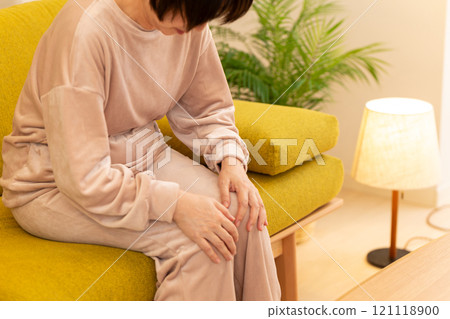 A middle-aged to senior woman suffering from cold feet in the living room on a winter night 121118900
