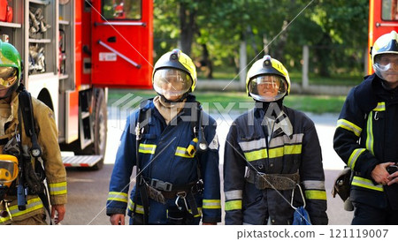 Portrait of male and female firefighters in helmets and protective uniforms standing near big red car. Young confident fireman and firewoman in full equipment posing against background of fire engine Portrait of male and female firefighters in helmets and protective uniforms standing near big red car. Young confident fireman and firewoman in full equipment posing against background of fire engine 121119007