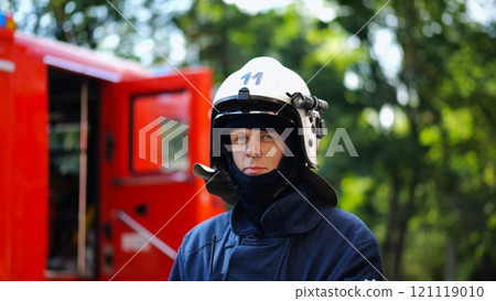 Portrait of confident male fireguard with dirty face standing near a fire engine. Young fireman in full equipment posing after fire against the background of big red truck. Concept of saving lives Portrait of confident male fireguard with dirty face standing near a fire engine. Young fireman in full equipment posing after fire against the background of big red truck. Concept of saving lives 121119010