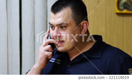 Male firefighter chief have serious telephone conversation with his subordinate by smartphone at fire station. Nervous fireman talking by mobile phone at fire department. Concept of heroic profession 121119019
