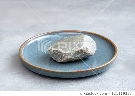 Gray stone on a blue plate on a light background. Copy space. 121119333