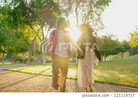 A Loving Couple Strolling Hand in Hand Through a Sunlit and Beautiful Park Together A Loving Couple Strolling Hand in Hand Through a Sunlit and Beautiful Park Together 121119757