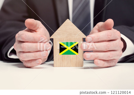 Businessman hand holding wooden home model with Jamaican flag. insurance and property concepts 121120014