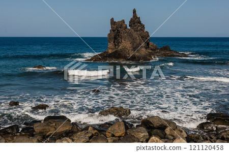 A dramatic coastal scene featuring a rugged rock formation surrounded by ocean waves A dramatic coastal scene featuring a rugged rock formation surrounded by ocean waves 121120458