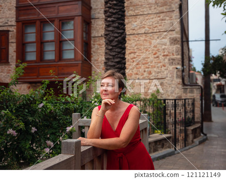 Woman in red dress walking narrow streets of old town Antalya during warm summer evening. Historic atmosphere and Mediterranean charm creates peaceful travel experience. Woman in red dress walking narrow streets of old town Antalya during warm summer evening. Historic atmosphere and Mediterranean charm creates peaceful travel experience. 121121149