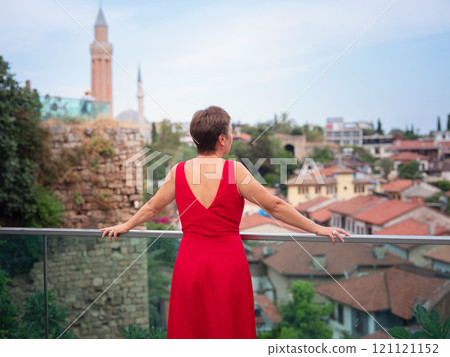 Woman in red dress walking narrow streets of old town Antalya during warm summer evening. Historic atmosphere and Mediterranean charm creates peaceful travel experience. view on Kalechi 121121152