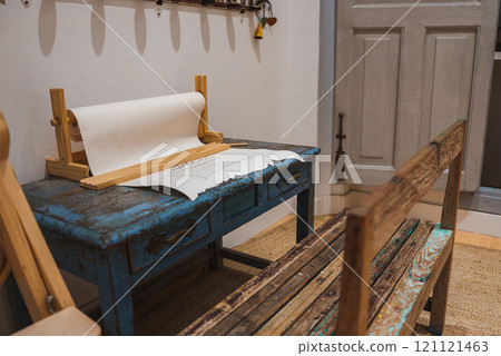 Interior features a distressed blue desk with ornate handles, a wooden paper roll holder, a simple bench, a textured rug, and a traditional wooden door. Interior features a distressed blue desk with ornate handles, a wooden paper roll holder, a simple bench, a textured rug, and a traditional wooden door. 121121463
