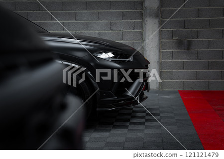 A Lamborghini Urus Performante with a matte black finish is showcased in a garage. The checkered black and red floor contrasts with the gray brick wall. 121121479