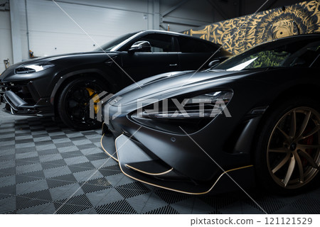 Two luxury supercars, Lamborghini Urus and McLaren 720S, parked indoors. The setting features a checkered floor and an artistic mural in the background. 121121529